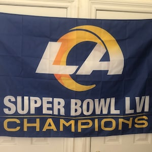 May include: A blue flag with a white and yellow "LA" logo and the text "SUPER BOWL LVI CHAMPIONS".