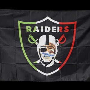 May include: A black rectangular flag featuring a central shield emblem with the text RAIDERS in white. The shield border is colored green, white, and red. Inside the shield is a stylized pirate figure wearing an eye patch and a helmet.