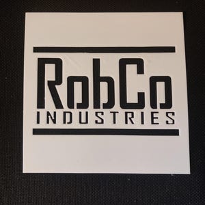 May include: A white square featuring the black text "RobCo INDUSTRIES" in a bold, sans-serif font. The text is centered and framed by horizontal black lines above and below the company name.