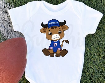 May include: White baby onesie with a cartoon buffalo wearing a blue and white football jersey with the number 17 and a blue hat that says "Buffalo".