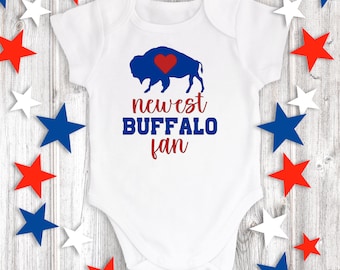May include: White baby onesie with a blue buffalo silhouette and a red heart. The text "newest BUFFALO fan" is printed in blue and red.