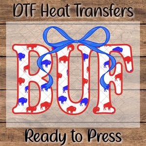 May include: DTF heat transfer design featuring the word "BUF" in red outline, filled with red and blue buffalo illustrations. A blue ribbon adorns the top. The text "Ready to Press" is at the bottom.