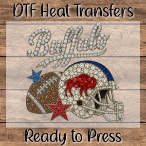 May include: DTF Heat Transfers design featuring a football, helmet, and stars with the word "Buffalo" in a sparkling font. The football is brown, the helmet is white and blue, and the stars are blue and red. The text "Ready to Press" is at the bottom.