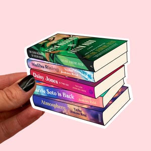 Puede incluir: Una pila de cinco libros de Taylor Jenkins Reid, cada uno con un diseño de portada único. Los títulos incluyen "The Seven Husbands of Evelyn Hugo", "Malibu Rising", "Daisy Jones & The Six", "Carrie Soto is Back" y "Atmosphere".