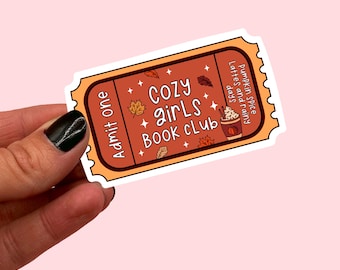 May include: A brown and orange ticket with the text "Cozy girls book club" and a drawing of a pumpkin spice latte. The ticket also says "Admit one" and "Pumpkin spice lattes and rainy days."