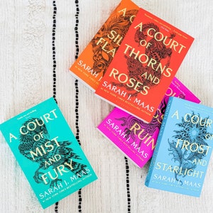 May include: A collection of five paperback books with colorful covers featuring intricate designs. The books are all part of the "A Court of Thorns and Roses" series by Sarah J. Maas. The titles include "A Court of Thorns and Roses", "A Court of Mist and Fury", "A Court of Wings and Ruin", "A Court of Frost and Starlight", and "A Court of Silver Flames".