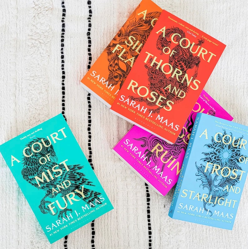 May include: A collection of five paperback books with colorful covers featuring intricate designs. The books are all part of the "A Court of Thorns and Roses" series by Sarah J. Maas. The titles include "A Court of Thorns and Roses", "A Court of Mist and Fury", "A Court of Wings and Ruin", "A Court of Frost and Starlight", and "A Court of Silver Flames".