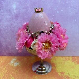 May include: A pink Easter egg with a gold crown and pink flowers in a silver pedestal.