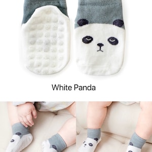 Puede incluir: Un par de calcetines blancos para beb&eacute; con un pu&ntilde;o gris y un dise&ntilde;o de cara de panda. Los calcetines tienen una parte inferior texturizada para agarre.