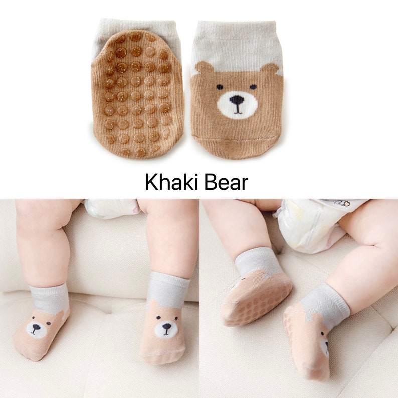 Puede incluir: Un par de calcetines para beb&eacute; con un dise&ntilde;o de oso marr&oacute;n y agarres antideslizantes en las suelas. Los calcetines son de color gris claro con detalles marrones. El texto "Khaki Bear" es visible debajo de los calcetines.