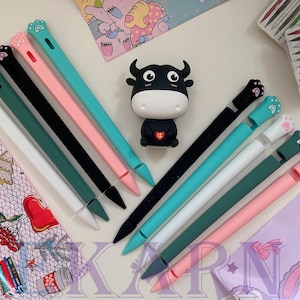 May include: Assortment of colorful silicone iPad stylus pen tips with paw print designs. The tips are arranged on a table with a small black and white bull figurine in the center.