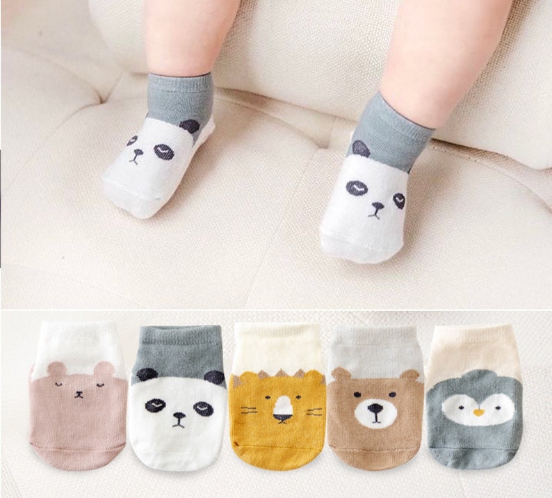 Puede incluir: Seis pares de calcetines para beb&eacute; con diferentes dise&ntilde;os de animales. Los calcetines son blancos con detalles en gris, marr&oacute;n, amarillo y azul. Los animales incluyen un panda, un oso, un le&oacute;n y un ping&uuml;ino.
