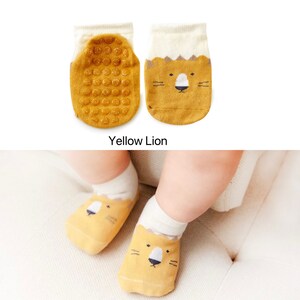 Puede incluir: Calcetines amarillos para beb&eacute; con un dise&ntilde;o de cara de le&oacute;n y puntos antideslizantes en la parte inferior. "Yellow Lion" est&aacute; escrito debajo de los calcetines.
