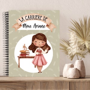 K&ouml;nnte beinhalten: Spiralgebundenes Notizbuch mit dem Text "LA CARRI&Egrave;RE DE Mme Ariane" &uuml;ber einer Illustration einer Lehrerin, die ein Buch h&auml;lt. Das Notizbuch hat einen hellgr&uuml;nen Hintergrund mit einem Bl&auml;ttermuster und einem Cartoon einer Lehrerin.