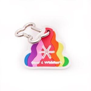 May include: A white, rainbow-coloured dog poo keychain with a silver bone-shaped clip. The keychain has a starburst design in the centre and the text "Char & Whiskers" at the bottom.