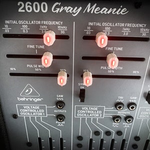 May include: A close-up of a grey Behringer 2600 Gray Meanie synthesizer with knobs and switches. The knobs are labelled "Initial Oscillator Frequency", "Fine Tune", and "Pulse Width". The switches are labelled "Sync On", "Saw", "Tri", and "Pulse".