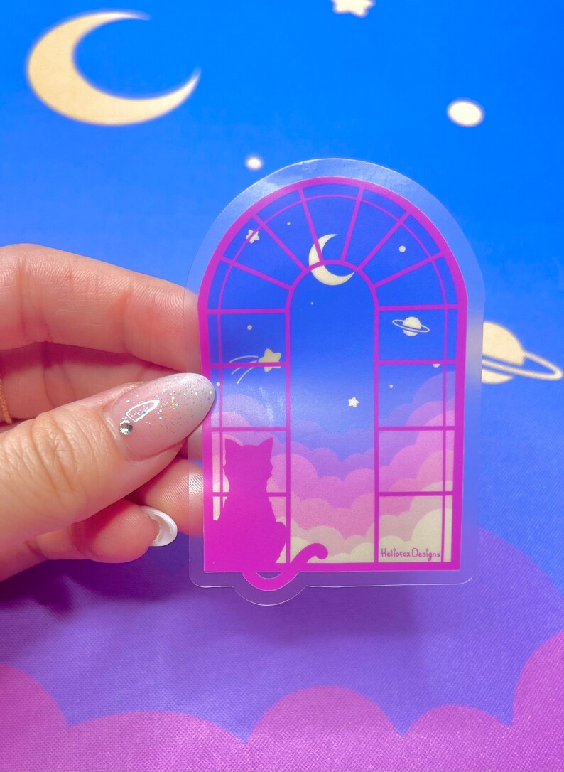 May include: A clear sticker with a pink silhouette of a cat looking out a window with a crescent moon and stars in the sky. The sticker has the text "Hallowee Designs" at the bottom.