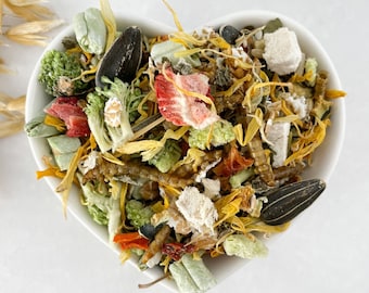 May include: A white heart-shaped bowl filled with a variety of dried fruits, vegetables, and seeds. The mix includes dried strawberries, sunflower seeds, and other ingredients.