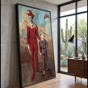 May include: A framed wall art print depicting two figures in jester costumes. The taller figure wears a solid red suit with a matching hat and white collar, while the shorter figure wears a diamond-patterned suit in red, blue, and white.
