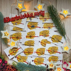 May include: A collection of red string bracelets with various silver charms, including a house, an airplane, an infinity symbol, a four-leaf clover, and a compass. The bracelets are displayed on white cards with the text "#skarbniczka_mry" and a website address.