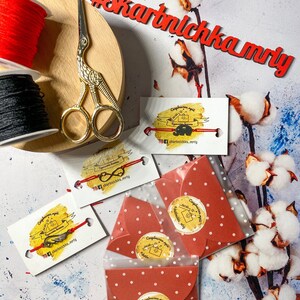 May include: Red and black string spools, gold scissors, and four red envelopes with white polka dots. Each envelope has a round sticker with a hand-drawn illustration of a key and the text "Сюрприз для тебя" in Russian, which translates to "Surprise for you". The envelopes are on a white background with cotton branches.