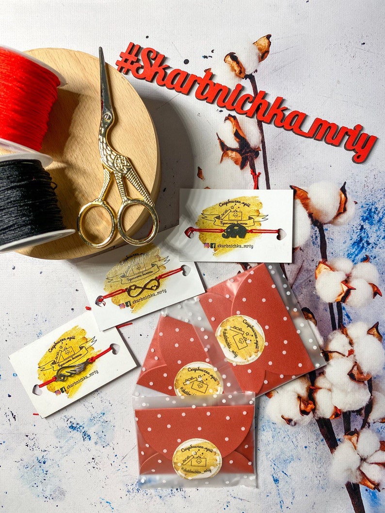 May include: Red and black string spools, gold scissors, and four red envelopes with white polka dots. Each envelope has a round sticker with a hand-drawn illustration of a key and the text "Сюрприз для тебя" in Russian, which translates to "Surprise for you". The envelopes are on a white background with cotton branches.