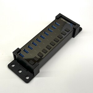 May include: A black USB hub with 10 ports and a SABRENT logo. The hub has a black plastic casing and is mounted on a wall.