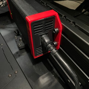 May include: A black and red power supply unit with a black power cord plugged into it. The power supply is mounted to a black metal surface.
