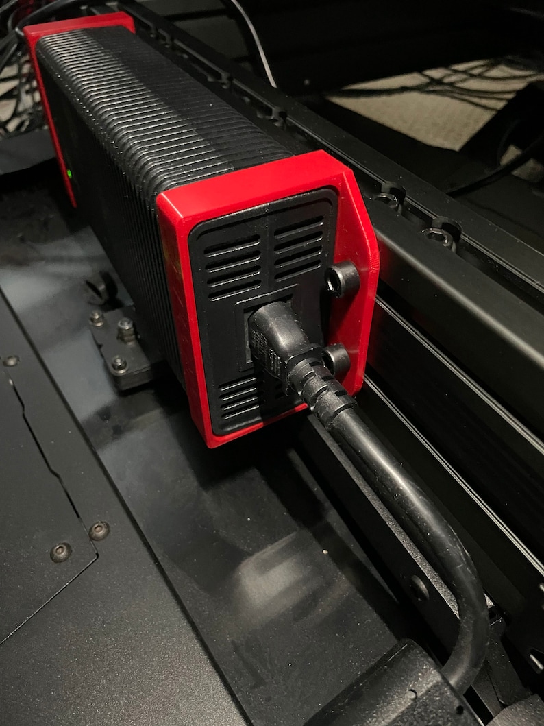 May include: A black and red power supply unit with a black power cord plugged into it. The power supply is mounted to a black metal surface.