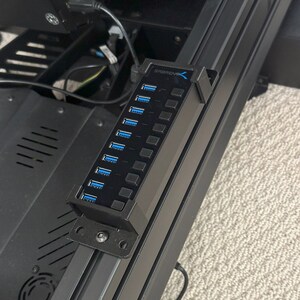May include: A black USB hub with the text "SABRENT" on it. The hub has 7 USB ports and is mounted to a black metal surface.