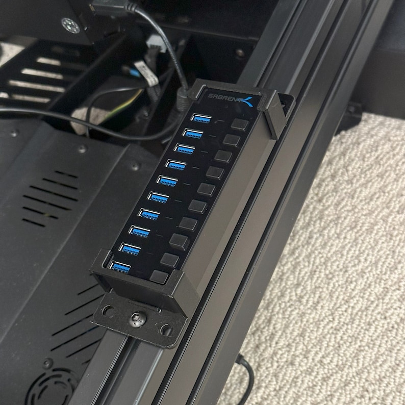 May include: A black USB hub with the text "SABRENT" on it. The hub has 7 USB ports and is mounted to a black metal surface.