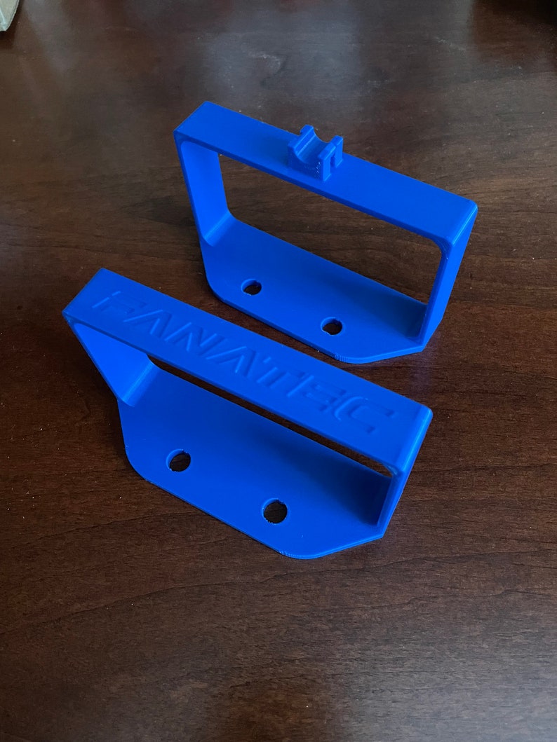 May include: Two blue plastic wall mounts with holes for screws. The bottom mount has the word "FANATEC" printed on it.