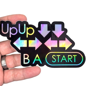May include: A black and iridescent sticker with the words "Up Up" and "BA START" and four arrows pointing in different directions.