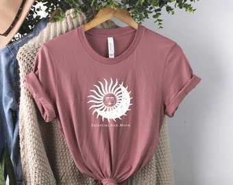 May include: A mauve t-shirt with a white graphic of a sun and moon with the text "Celestial Sun. Moon".