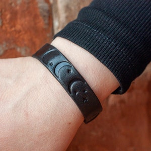 May include: A black leather bracelet with a moon and star design.