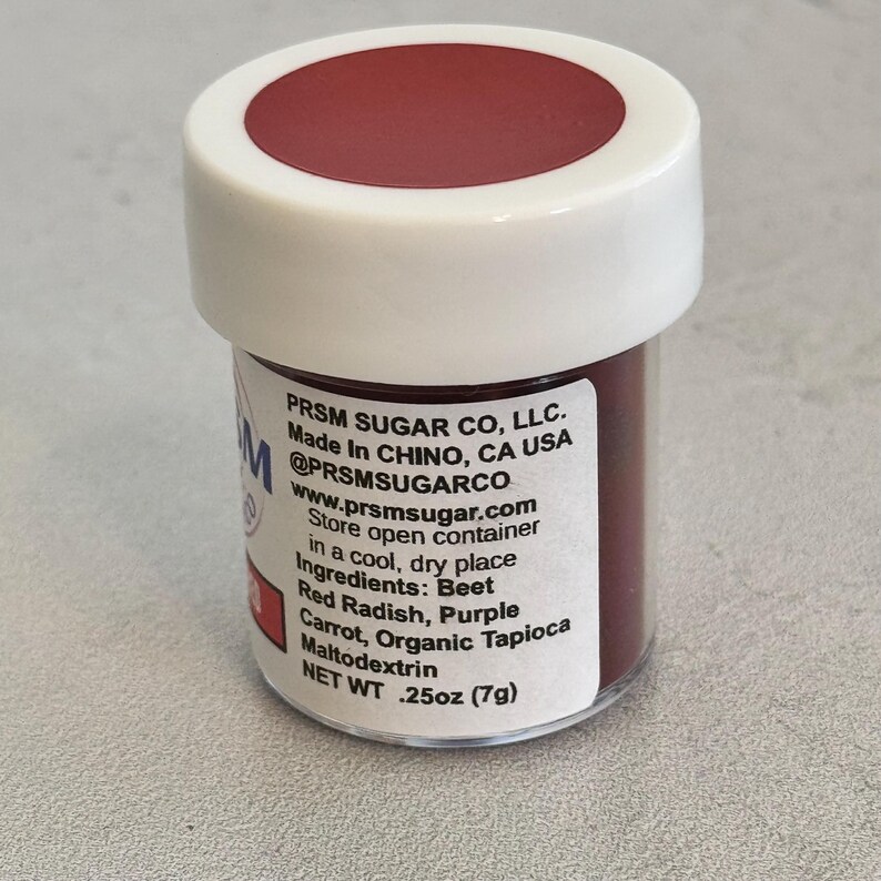 May include: A small, white jar with a red lid filled with red food coloring. The label reads "PRSM SUGAR CO, LLC. Made In CHINO, CA USA @PRSMSUGARCO www.prsmsugar.com Store open container in a cool, dry place Ingredients: Beet Red Radish, Purple Carrot, Organic Tapioca Maltodextrin NET WT .25oz (7g)"