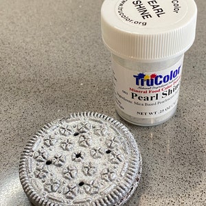 May include: A small jar of TruColor Pearl Shine mineral food color powder. The jar is white with a black label and the text "TruColor Pearl Shine" is printed on the label. The jar is sitting on a gray surface next to a silver-colored Oreo cookie.