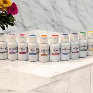 以下が含まれることがあります： 黒、紫、ピンク、青、オレンジ、赤、黄、緑、茶色など、さまざまな色の液体食用色素が入った小さなボトルが10本あります。ボトルには「PRSM」と「液体食用色素」の文字が書かれています。