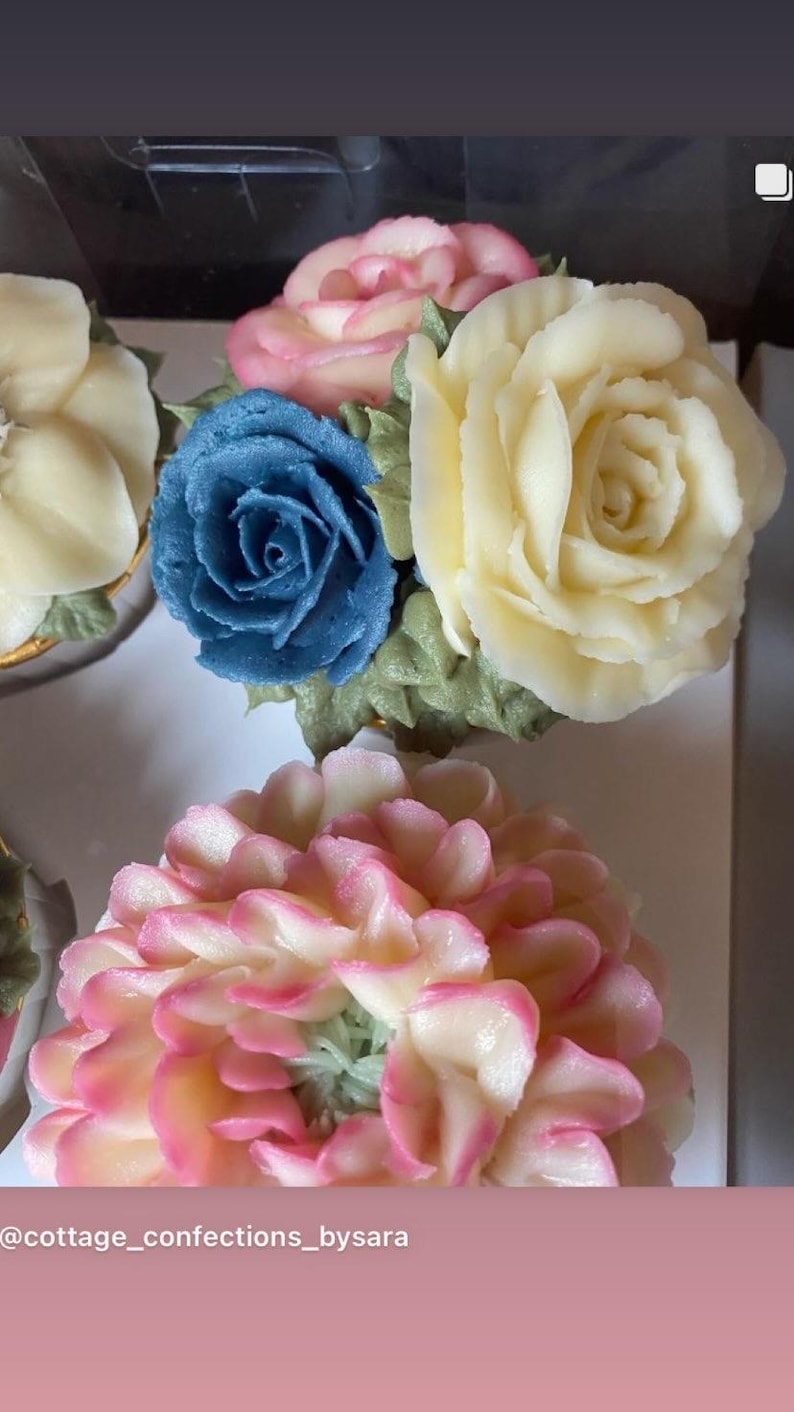 May include: Close-up of cupcakes decorated with buttercream flowers. The cupcakes feature a variety of colours, including pink, blue, and yellow. The flowers are intricately detailed, resembling roses and other blooms. The text "@cottage_confections_bysara" is visible.