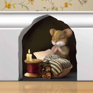 Pode incluir: Um rato castanho com os olhos fechados está rezando em um pequeno espaço semelhante a uma caverna. O rato está sentado em uma cama com um cobertor listrado e um pequeno urso de pelúcia. Uma vela acesa e um carretel de fio vermelho estão em uma mesa ao lado da cama.