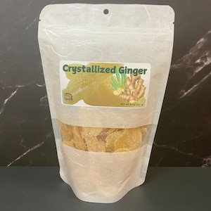 May include: A white resealable bag filled with crystallized ginger. The bag has a label that says "Crystallized Ginger" and "Net Wt 8 oz (227 g)".