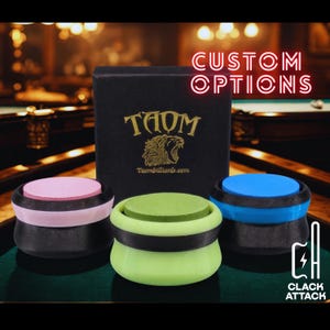 May include: Three pool cue chalk holders in pink, green, and blue, with black accents. A black box with gold text and a tiger logo is behind them. The text "CUSTOM OPTIONS" and "CLACK ATTACK" are also visible.