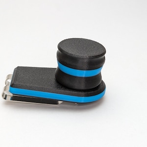 May include: A black and blue money clip with a textured surface. The clip has a rectangular base with a curved top and a cylindrical top. The clip is accented with a bright blue stripe.