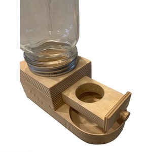 Peut inclure: Un distributeur de nourriture pour animaux en bois avec un bocal en verre pour la nourriture s&egrave;che et un tiroir coulissant pour la distribution de la nourriture. Le distributeur est en bois clair et a une finition naturelle.