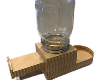 May include: A wooden pet feeder with a clear glass jar for holding food or water. The feeder has a slide-out tray for easy access to the food or water. The feeder is made of natural wood and has a simple, rustic design.