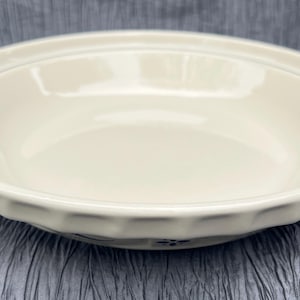 May include: Off-white ceramic serving bowl with a fluted rim and a dark blue accent line. The bowl has a simple, classic design, suitable for serving various dishes. The bowl's diameter is approximately 10 inches.