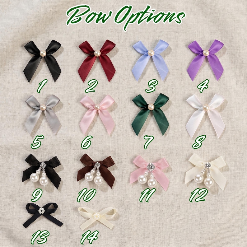 Op de afbeelding: Een collectie van veertien satijnen lintstrikken genummerd van 1 tot 14. De strikken zijn verkrijgbaar in diverse kleuren zoals zwart, rood, blauw, paars, grijs, roze, groen en wit, en zijn voorzien van enkele parels of bungelende parelbedels.