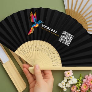 Puede incluir: Abanico plegable negro con un colorido diseño de colibrí y el texto "YOUR LOGO FREEDOM ANIMAL" y un código QR. El abanico tiene un mango de madera natural y está parcialmente abierto, revelando su diseño plisado.
