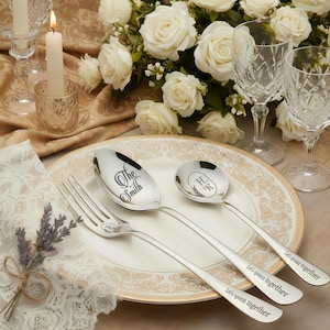 May include: A formal table setting with silverware, a plate, and floral arrangements. The silverware includes a fork, a large spoon engraved with "The Smith", and a smaller spoon with initials. The spoons have the phrase "Let's spoon together" engraved on the handles.