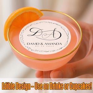 May include: A cocktail in a gold-rimmed glass with an orange slice garnish. The drink is a pale orange colour and features a circular edible design with the initials "DA" and the names "David & Amanda" with the date "02.14.2023". The text "Edible Design - Use on Drinks or Cupcakes!" is at the bottom.